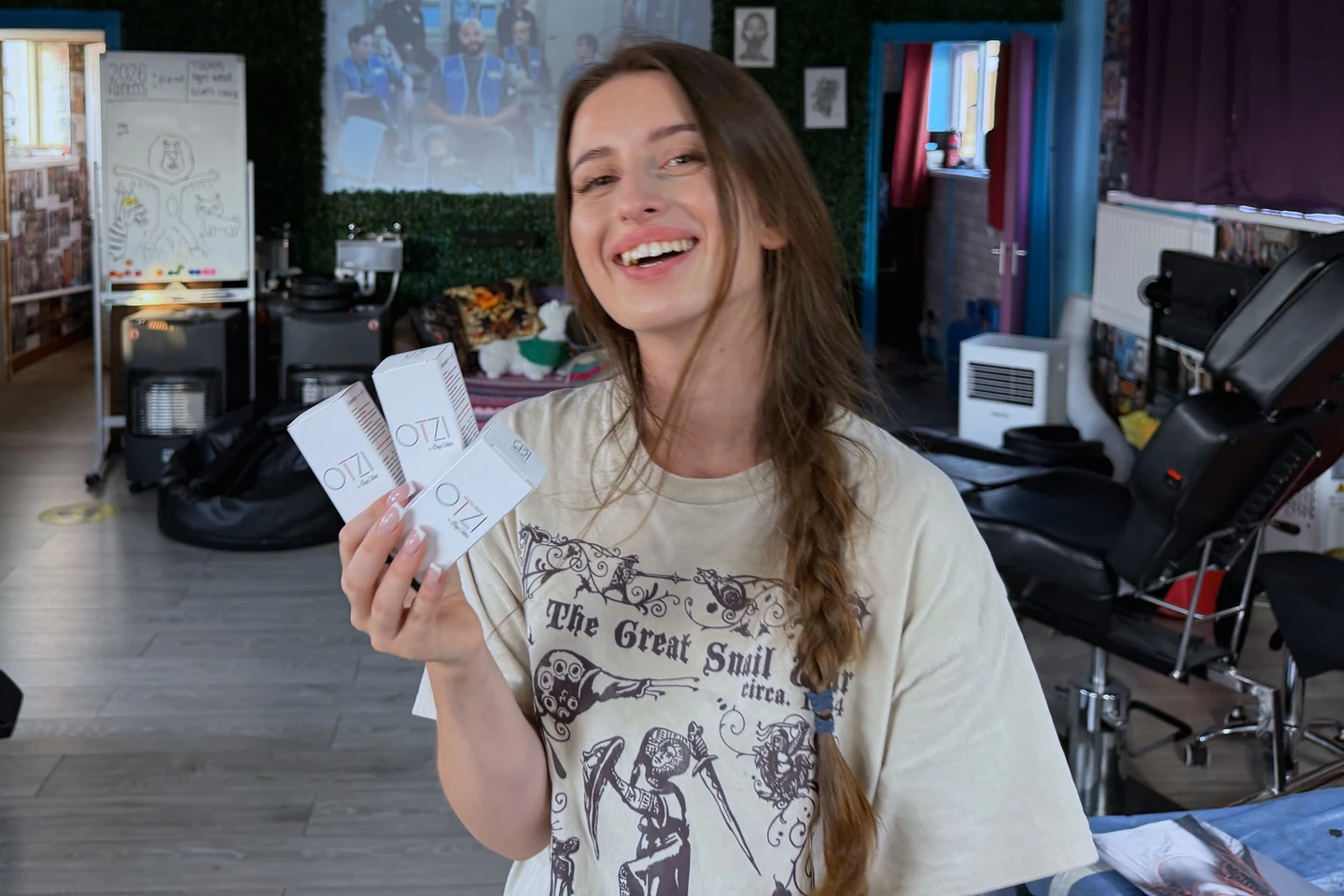 Domi laughing in her studio at Tattooed Llama, holding OTZI tattoo aftercare kits