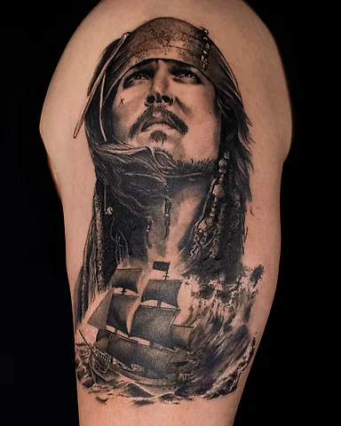 Realistic black and grey Jack Sparrow portrait and pirate ship upper arm tattoo, by Domi (based in Coventry, UK)