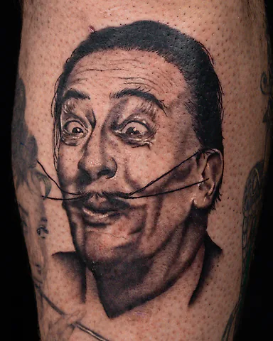 Realistic black and grey Salvador Dalí portrait shin tattoo, by Domi (based in Coventry, UK)